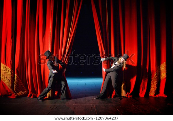 Actor and\
actress in tuxedos open theater\
curtain