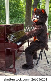 actor dressed as bear entertains playing piano on the bandstand in the park