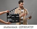 Actor performing while second assistant camera holding clapperboard on grey background