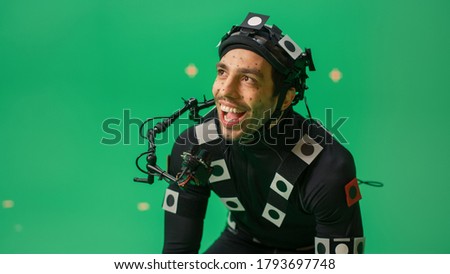 Actor Wearing Motion Caption Suit and Head Rig acts as an Animal or a Monster for CGI Green Screen Scene. Big Budget Filmmaking On Film Studio Set Shooting Blockbuster Movie with Chroma Key.