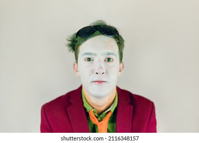 Actor With White Makeup On Face And Green Eyes And Hair. Paint Of Clown Or Mime. Person In Suit With Yellow Stripes Tie Looks At Camera. Theater Concept. Black Glasses On Head.