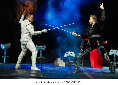 Actors In Black And White Clothes With Woman In Red Dress Play A Duel With Swords Performance On The Theater Stage