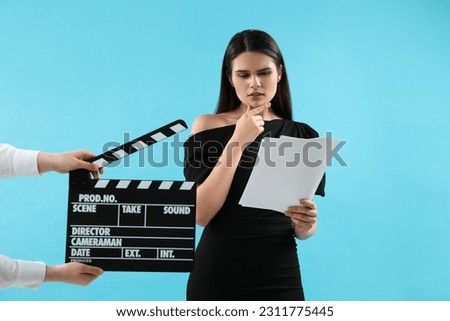 Actress performing role while second assistant camera holding clapperboard on light blue background. Film industry