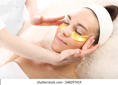 Acupressure, Massage His Temples, Golden Flakes Collagen.Cosmetic Procedure, The Woman's Face With Gold Flakes Under The Eyes And On The Lips 