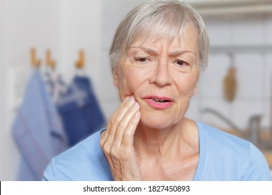 Acute toothache: senior woman in her kitchen with a hand at her painful jaw. - Powered by Shutterstock