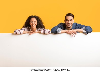 Ad Banner. Smiling Arab Couple Leaning At Blank White Advertisement Board, Happy Young Middle Eastern Man And Woman Demonstrating Copy Space For Your Design, Posing Over Yellow Background - Shutterstock ID 2207807431