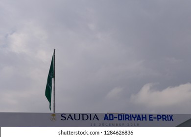 AD DIRIYAH, SAUDI ARABIA – DECEMBER 15, 2018: The Logo Of The SAUDIA Ad Diriyah FIA Formula E E-Prix Race With The Flag Of Saudi Arabia In The Background