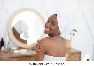 Ad Of Healthy And Beauty Care, Moisture Dry Skin And Spa Treatment. Happy Millennial African American Female In Towel Smears Body Cream After Shower, Turns And Looks At Camera In Bedroom In Morning