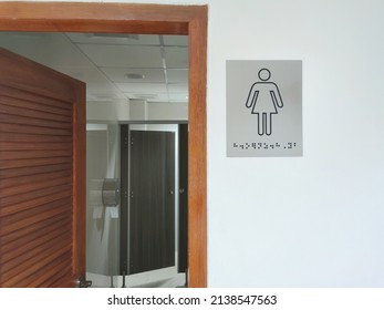 ADA Compliant Signs For Womens Restroom With Braille And Female Gender Symbol. Public Female Restroom With Female Toilet Sign On White Wall.