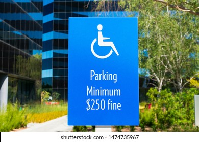 ADA Handicapped Sign With Handicapped Wheelchair Symbol) Marks Accessible Parking Space  On Outdoor Parking Lot. Minimum Fine $250 Warning Sign. Green Landscaping And Office Buildings In Background