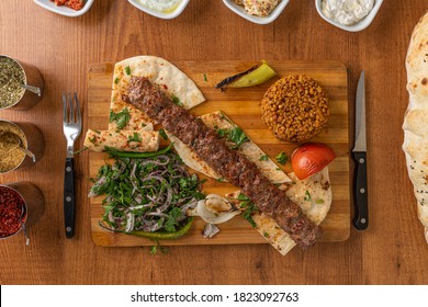 Adana/Urfa Kebab served with onions, bulgur rice on a wooden plate - Shutterstock ID 1823092763
