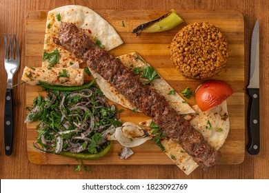 Adana/Urfa Kebab served with onions, bulgur rice on a wooden plate - Shutterstock ID 1823092769