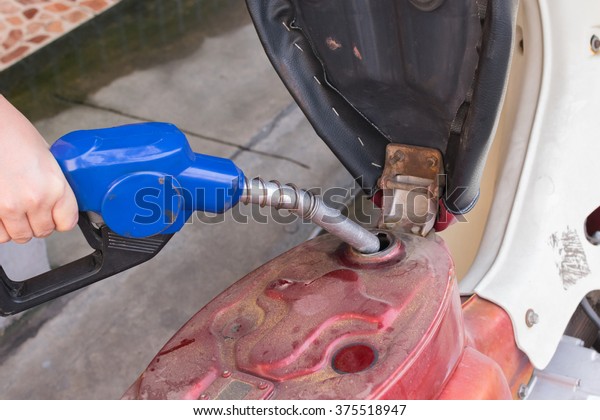 Add benzine fuel to motorcycle at a gasoline station\
with a hand