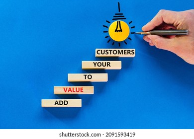Add value to your customers symbol. Concept words 'Add value to your customers' on wooden blocks on a blue background. Light bulb icon. Businessman hand with pen. Business, customers value concept.