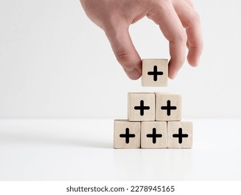 Added value or increasing benefits concept. Progress and profit to benefit growth and development in business. Hand places cube with plus symbol on top of the wooden cube pyramid.
