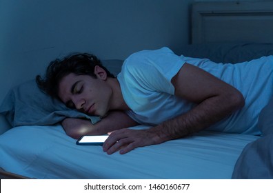 Пристрастие к социальным сетям молодой человек засыпает со смартфоном ночью в постели. Образ жизни человека, спящего в темной спальне с включенным мобильным экраном. Зависимость от мобильного использования.
