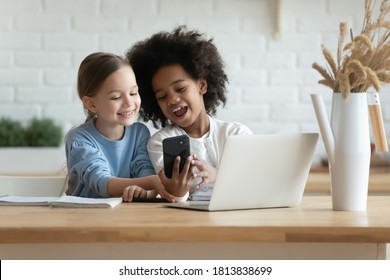 Addicted To Technology Overjoyed Little Mixed Race Kids Sisters Looking At Mobile Phone Scree, Using Funny Photo Application, Recording Video For Social Networks Or Playing Online Games At Home.