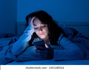 Addicted young woman chatting and surfing on the internet using her smart phone sleepy, bored and tired late at night. Dramatic dark light. In Internet, Mobile addiction and insomnia concept. - Shutterstock ID 1451180516