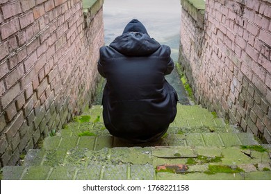 Addiction Concept. A Drug Addict In A Hood Sits In An Abandoned House After Taking Drugs. Fighting Addiction, View From The Back.