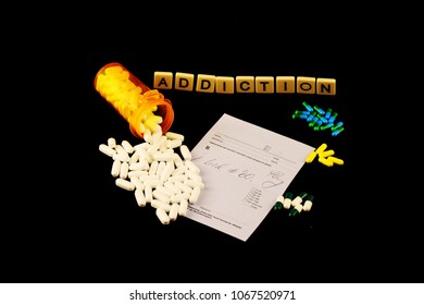 Addiction Spelled Out With Tiles Above Spilled White Pills Over A Prescription Pad And Colored Pills On A Black Background