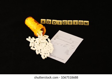 Addiction Spelled Out With Tiles, Spilled White Prescription Pills Over A Prescription Pad On A Black Background