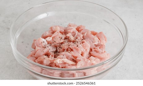 Adding black pepper to chopped chicken fillet . Glass bowl with the chopped marinated chicken meat close-up on kitchen tgable