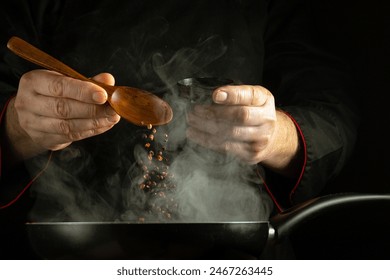 Adding dry pepper to a hot frying pan with a spoon in the cook hand. Cooking concept on black background. - Powered by Shutterstock