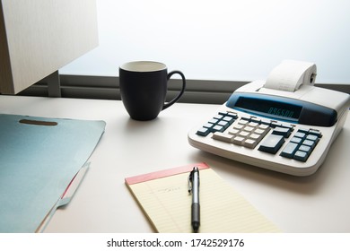 Adding machine with coffee cup, notepad, and filefolder on office desk