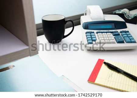 Adding machine with coffee cup, notepad, and filefolder on office desk