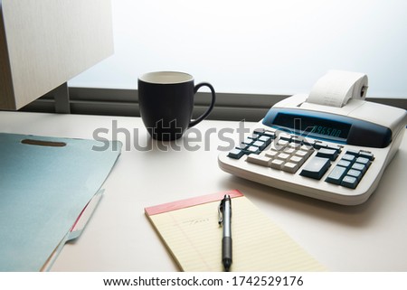 Adding machine with coffee cup, notepad, and filefolder on office desk