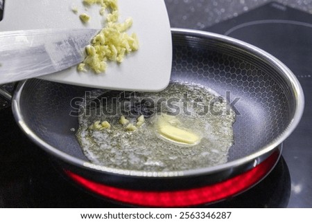adding minced garlic to melted butter in a frying pan on a hot stovetop