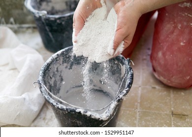 Adding The Plaster Powder To The Water In A Mixing Container By Sprinkling Or Sifting The Powder Over The Water. Preparing Plaster Mix With Sculptor Bare Hands. Basic, Essential Sculpting Supplies.