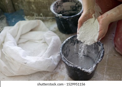 Adding The Plaster Powder To The Water In A Mixing Container By Sprinkling Or Sifting The Powder Over The Water. Preparing Plaster Mix With Sculptor Bare Hands. Basic, Essential Sculpting Supplies.