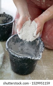 Adding The Plaster Powder To The Water In A Mixing Container By Sprinkling Or Sifting The Powder Over The Water. Preparing Plaster Mix With Sculptor Bare Hands. Basic, Essential Sculpting Supplies.