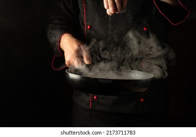 Adding Salt To Meat Steaks In A Hot Pan With Steam In The Hands Of A Professional Chef. Cooking Meat Patties For A Burger