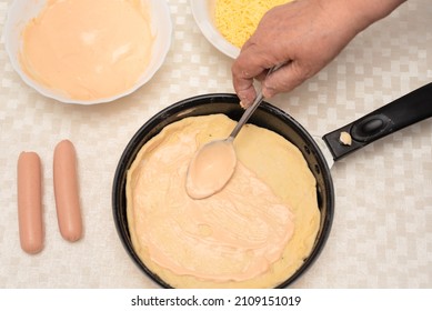 Adding Sauce On The Raw Dough On Black Pan For Homemade Pizza By Senior Woman. Other Ingredients Are On The Table. Top View With Selective Focus. Process Of Cooking Pizza, Step 4