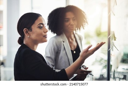 Adding Structure To Their Ideas. Shot Of Two Businesswomen Brainstorming With Notes On A Glass Wall In An Office.