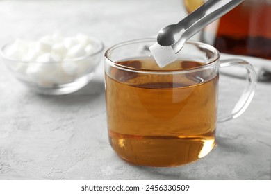 Adding sugar cube into cup of tea at grey textured table, closeup