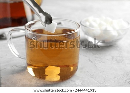 Adding sugar cube into cup of tea at grey textured table, closeup