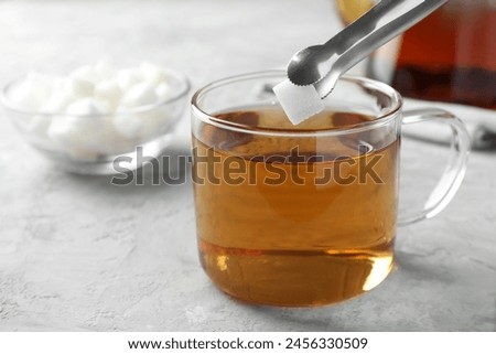 Adding sugar cube into cup of tea at grey textured table, closeup