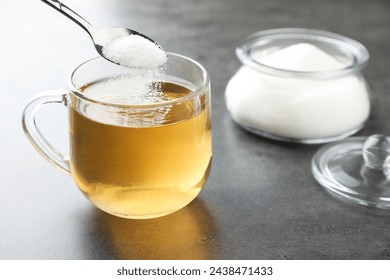 Adding sugar into aromatic tea at grey table, closeup