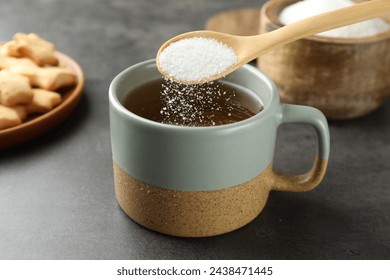 Adding sugar into aromatic tea at grey table, closeup