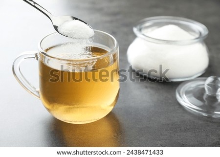 Adding sugar into aromatic tea at grey table, closeup