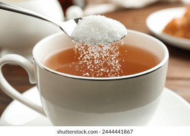 Adding sugar into cup of tea at table, closeup