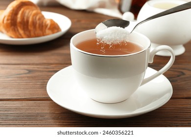 Adding sugar into cup of tea at wooden table, closeup