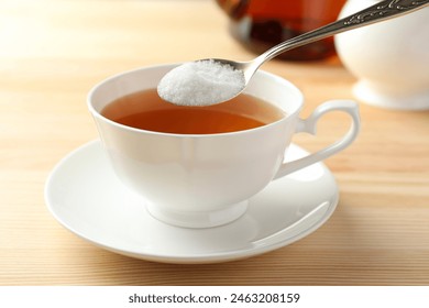 Adding sugar into cup of tea at wooden table, closeup