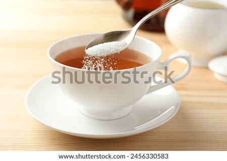 Adding sugar into cup of tea at wooden table, closeup