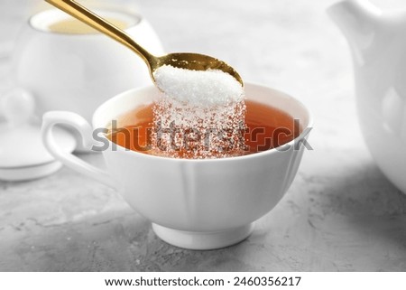Adding sugar into cup of tea at grey textured table, closeup