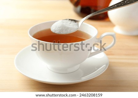 Adding sugar into cup of tea at wooden table, closeup