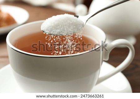 Adding sugar into cup of tea at table, closeup